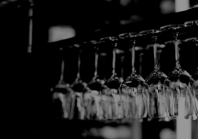 Black and white image of glasses hanging from a bar glass holder.